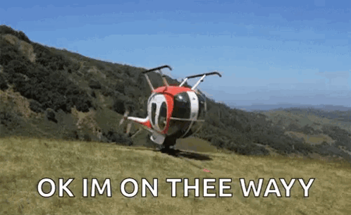 A Helicopter Is Sitting On Top Of A Grassy Hill With The Words Ok Im On Thee Wayy Written On It . GIF