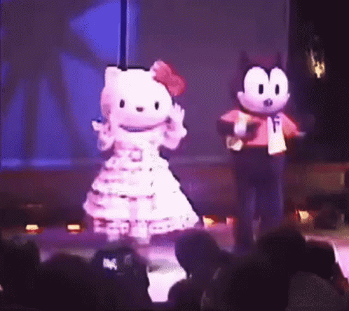 A Hello Kitty Mascot And Felix The Cat Mascot Are Dancing On A Stage In Front Of A Crowd . GIF