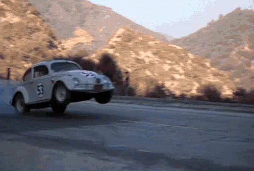 A Herbie The Beetle Is Driving Down A Road With Mountains In The Background GIF
