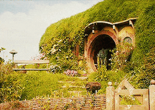 A Hobbit House Sits On Top Of A Hill With A Wooden Gate In Front Of It GIF