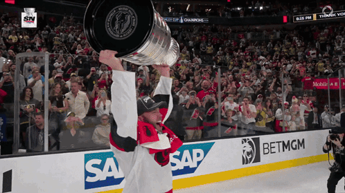A Hockey Player Holds Up A Trophy In Front Of A Crowd With Sap And Betmgm Advertisements GIF
