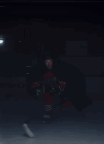 A Hockey Player In A Red And Black Uniform Is Holding A Hockey Stick GIF