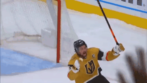 A Hockey Player Is Holding A Hockey Stick In The Air In Front Of A Goal . GIF