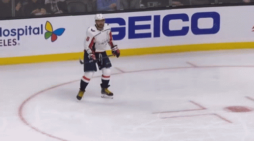 A Hockey Player Is Standing On The Ice In Front Of A Sign For Geico GIF