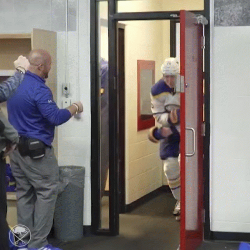 A Hockey Player Is Walking Through A Door With A Sabres Logo On The Wall Behind Him GIF