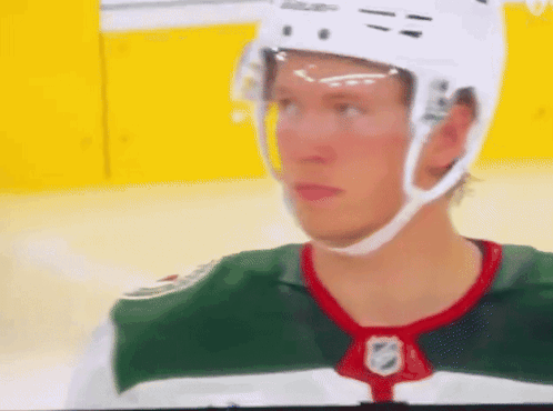 A Hockey Player Is Wearing A White Helmet And A Green And White Jersey GIF