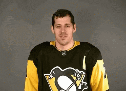 A Hockey Player Wearing A Black And Yellow Jersey With A Penguin On It Is Standing In Front Of A Gray Background . GIF