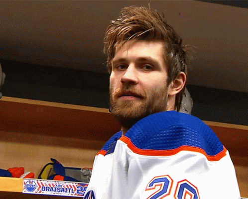 A Hockey Player With The Number 20 On His Jersey Stands In A Locker Room GIF