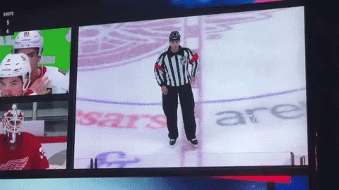 A Hockey Referee Is Standing On The Ice In Front Of A Sign That Says Shots GIF
