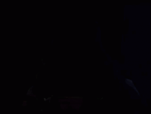 A Hooded Figure In A Dark Room With A Red And Black Mask GIF