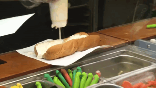 A Hot Dog With Mayonnaise Being Poured On It Sits On A Counter GIF