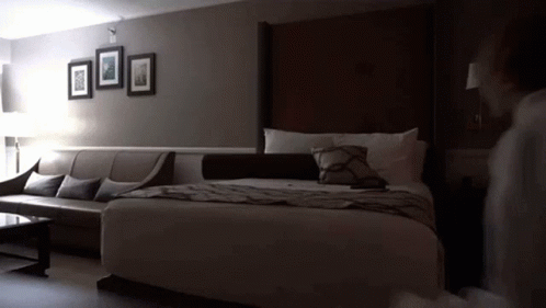 A Hotel Room With A King Size Bed A Couch And A Coffee Table GIF