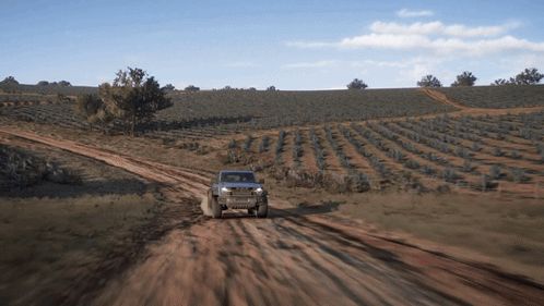A Jeep Is Driving Down A Dirt Road With A Field In The Background GIF