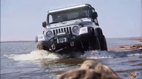 A Jeep Is Driving Through A Body Of Water With A Few Rocks In The Foreground GIF