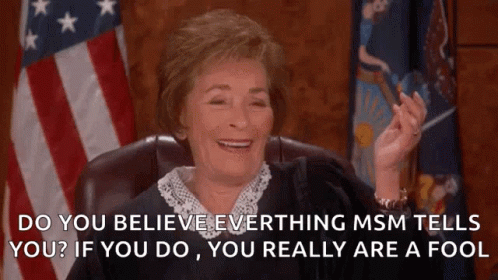 A Judge Is Smiling In Front Of An American Flag While Sitting In A Chair . GIF