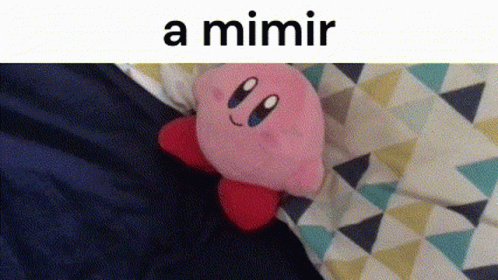 A Kirby Stuffed Animal Is Laying On A Bed Next To A Triangle Patterned Blanket . GIF