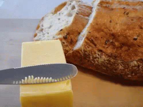 A Knife Is Cutting A Piece Of Butter Next To A Slice Of Bread GIF