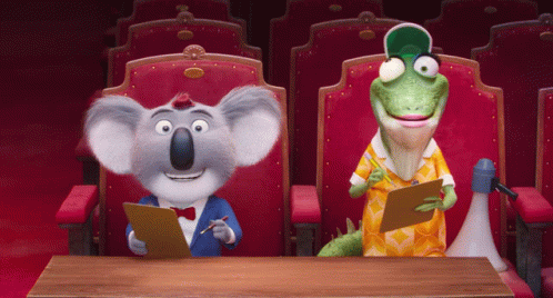 A Koala And A Lizard Are Sitting At A Table In A Theater GIF