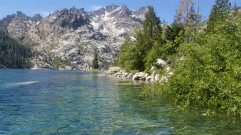 A Lake With Mountains In The Background Is Surrounded By Trees And Rocks GIF