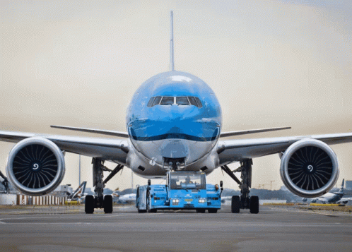 A Large Blue And White Airplane Is Being Towed By A Blue Vehicle GIF