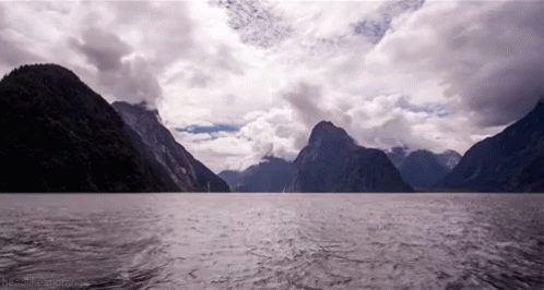 A Large Body Of Water Surrounded By Mountains And A Cloudy Sky GIF