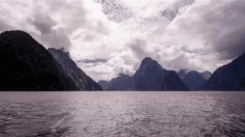 A Large Body Of Water Surrounded By Mountains And Clouds GIF