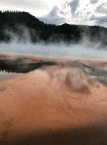 A Large Body Of Water With Mountains In The Background And Smoke Coming Out Of The Water GIF