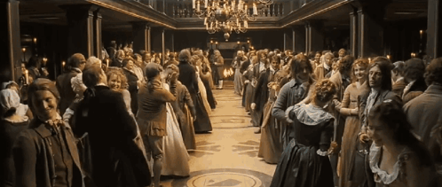A Large Crowd Of People Are Dancing In A Ballroom With A Chandelier GIF
