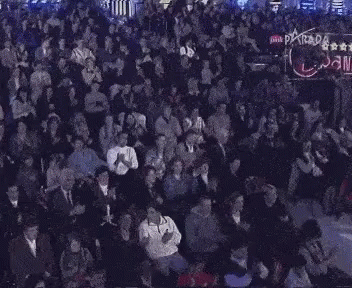 A Large Crowd Of People Are Sitting In A Dark Room With The Word Parada On The Bottom GIF