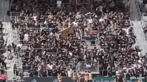 A Large Crowd Of People Are Sitting In A Stadium Watching A Soccer Game . GIF
