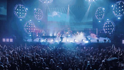 A Large Crowd Of People Are Watching A Band On Stage GIF