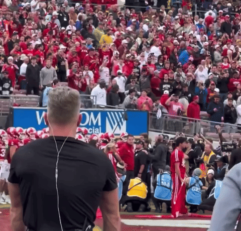 A Large Crowd Of People Watching A Football Game In Front Of A Sign That Says Wom GIF