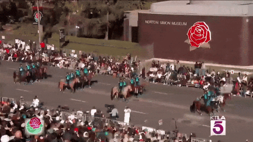 A Large Crowd Of People Watching A Parade In Front Of A Building That Says Norton Simon Museum GIF