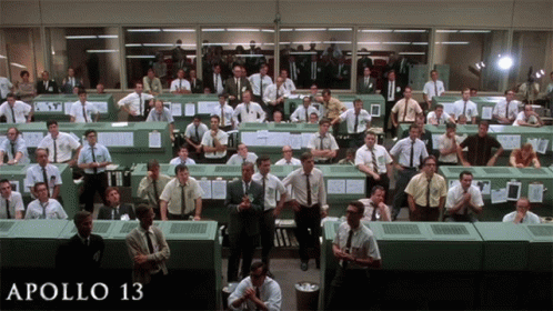 A Large Group Of Men Are Gathered In A Room With The Words Apollo 13 On The Bottom Right GIF