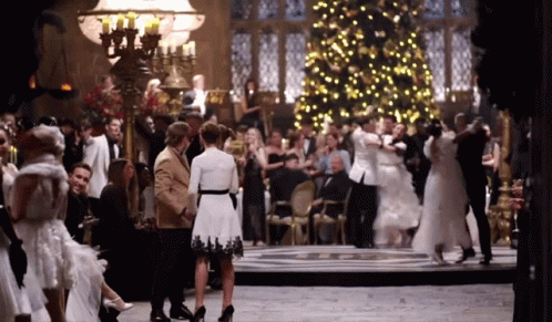 a large group of people are dancing in a room with a christmas tree in the background