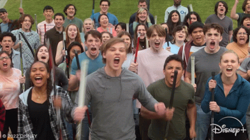 A Large Group Of People Are Holding Bats And Screaming In Front Of A Disney+ Logo GIF