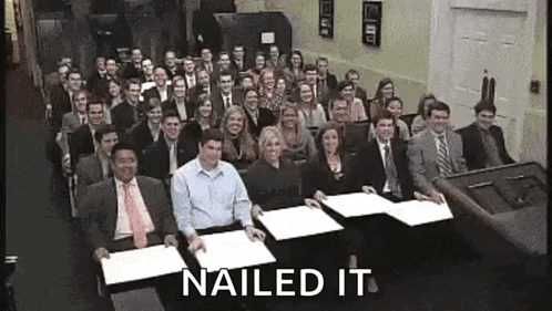 A Large Group Of People Are Sitting At Tables With Papers In Front Of Them And The Words Nailed It Are Above Them . GIF