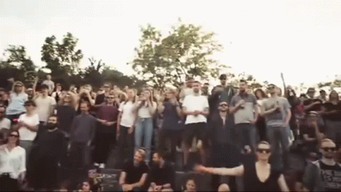 A Large Group Of People Are Standing In A Stadium With Their Arms In The Air . GIF