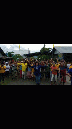 A Large Group Of People Are Standing In Front Of A Building Holding Their Hands Up In The Air . GIF