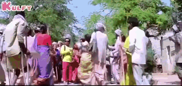 A Large Group Of People Are Walking Down A Street In A Village . GIF