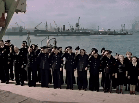 a large group of people in black uniforms salute in front of a body of water