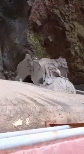 A Large Rock Is Sitting On The Side Of A Road Next To A Waterfall . GIF