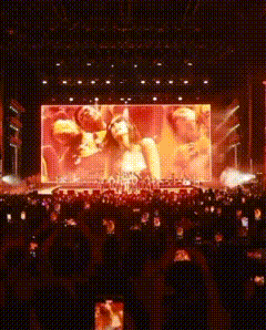A Large Screen Shows A Group Of People On A Stage At A Concert GIF
