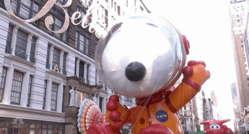 A Large Snoopy Balloon Is In Front Of A Building That Says Nbc On It GIF