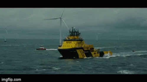 A Large Yellow Ship Is Floating In The Ocean With A Wind Turbine In The Background GIF