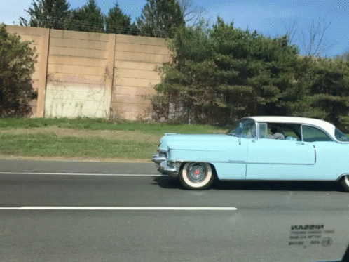 A Light Blue Car Is Driving Down A Highway With A Sticker On The Windshield That Says Happy GIF