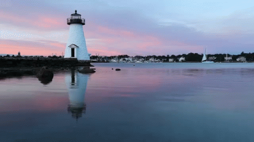 A Lighthouse In The Middle Of A Body Of Water At Sunset GIF