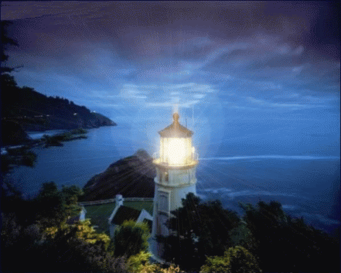 A Lighthouse On A Hill Overlooking A Body Of Water At Night GIF