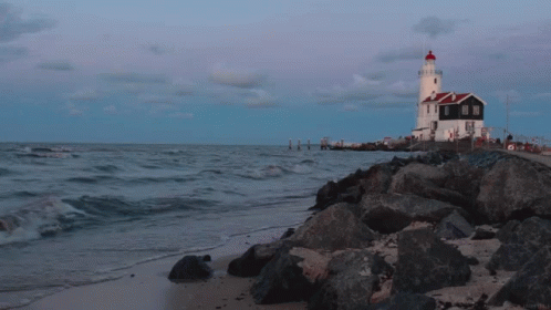 A Lighthouse Sits On A Rocky Shoreline Near The Ocean GIF