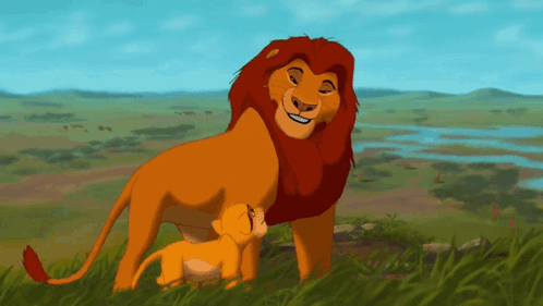 A Lion And A Cub Standing In The Grass GIF